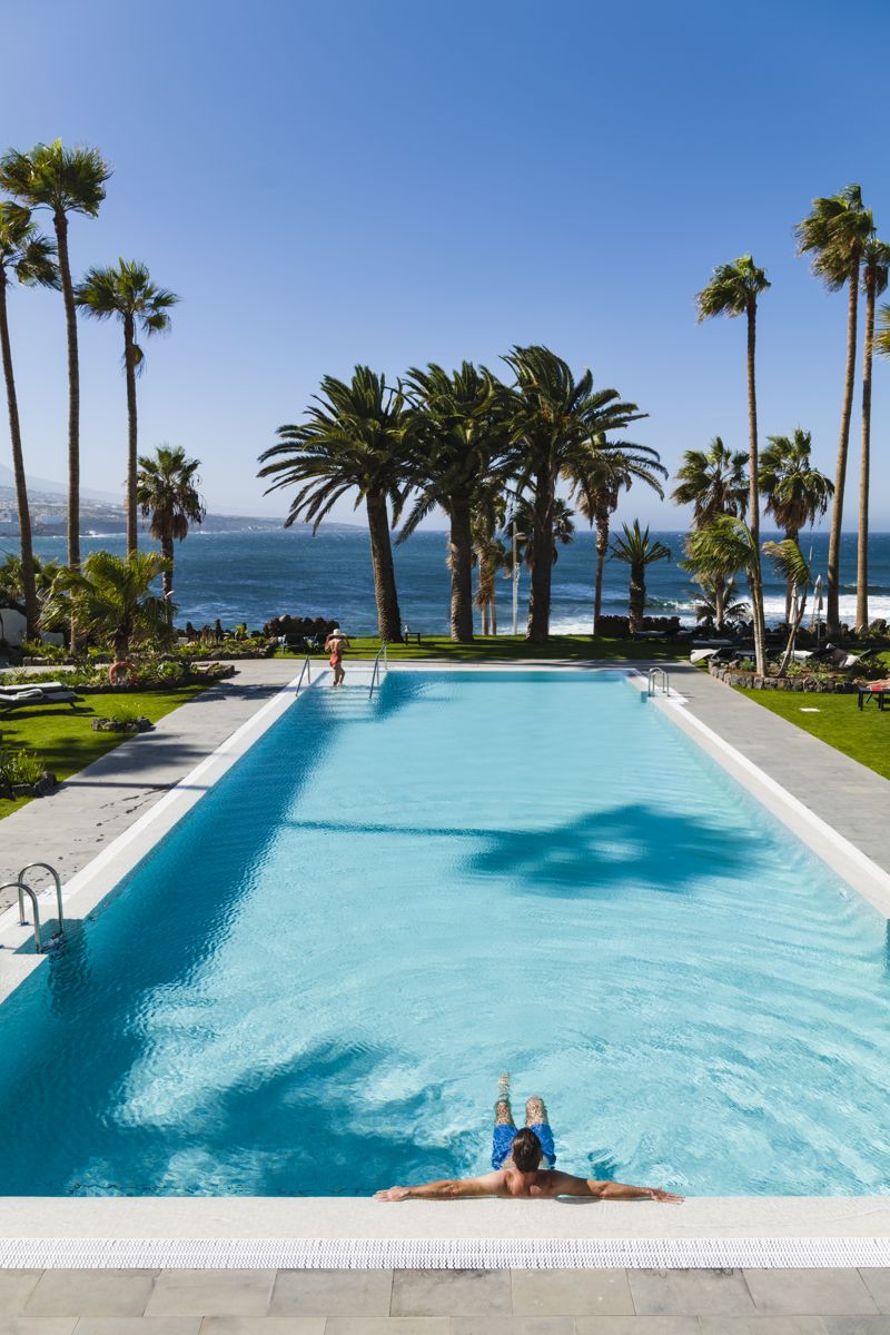 Mann entspannt sich im Pool mit Blick auf das Meer in Puerto de la Cruz, Teneriffa.