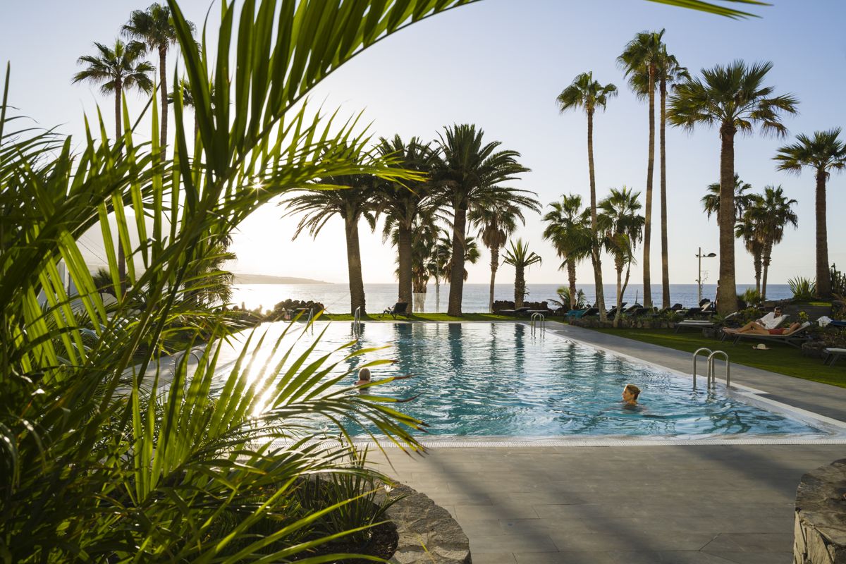 Pool mit Palmen am Meer bei Sonnenuntergang in Costa Adeje, Teneriffa.