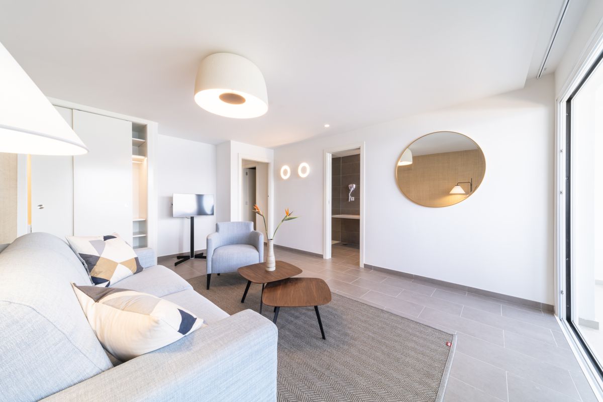 Helles Wohnzimmer mit Sofa, Sessel, Couchtisch und Spiegel in einem Hotelzimmer in Teneriffa.