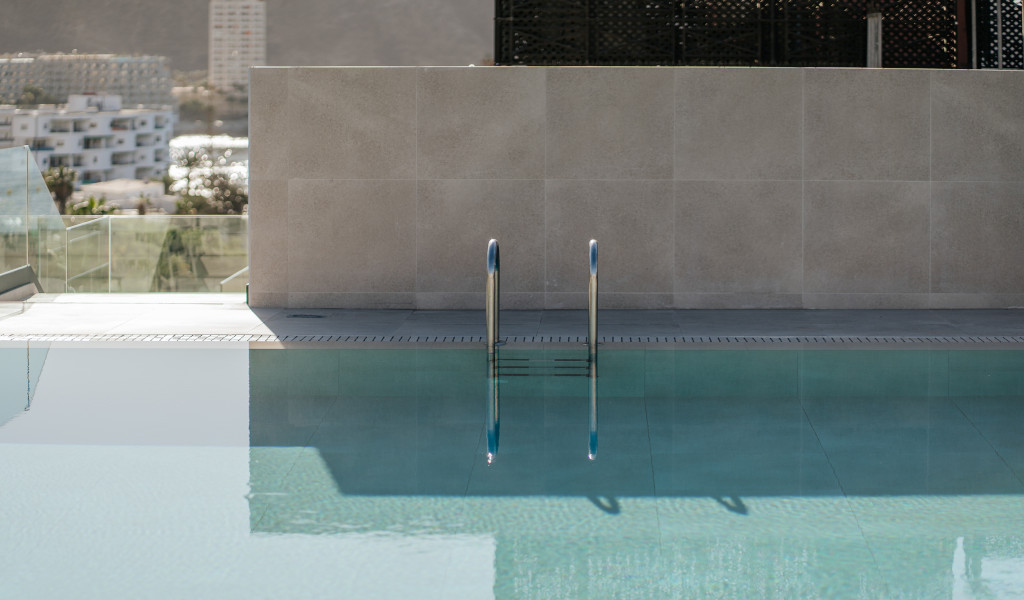 Pool mit Geländer im Freien in Adeje, Teneriffa. Im Hintergrund Gebäude.