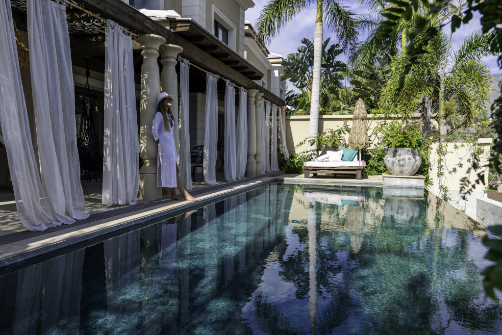 Frau in weißem Kleid steht neben Pool in sonniger Villa in Teneriffa.
