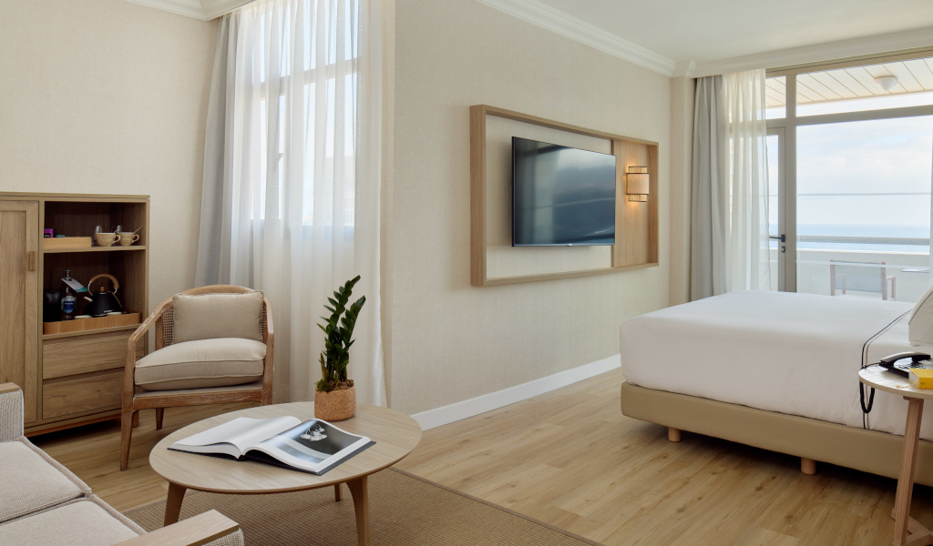 Schlafzimmer mit Bett, Fernseher, Sessel und Meerblick in einem Hotel auf Teneriffa.