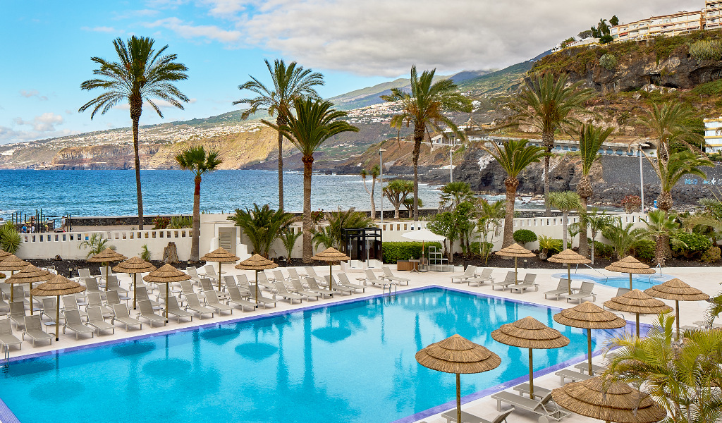 Pool mit Liegen und Palmen, Blick auf Meer und Berge in Puerto de la Cruz, Teneriffa.