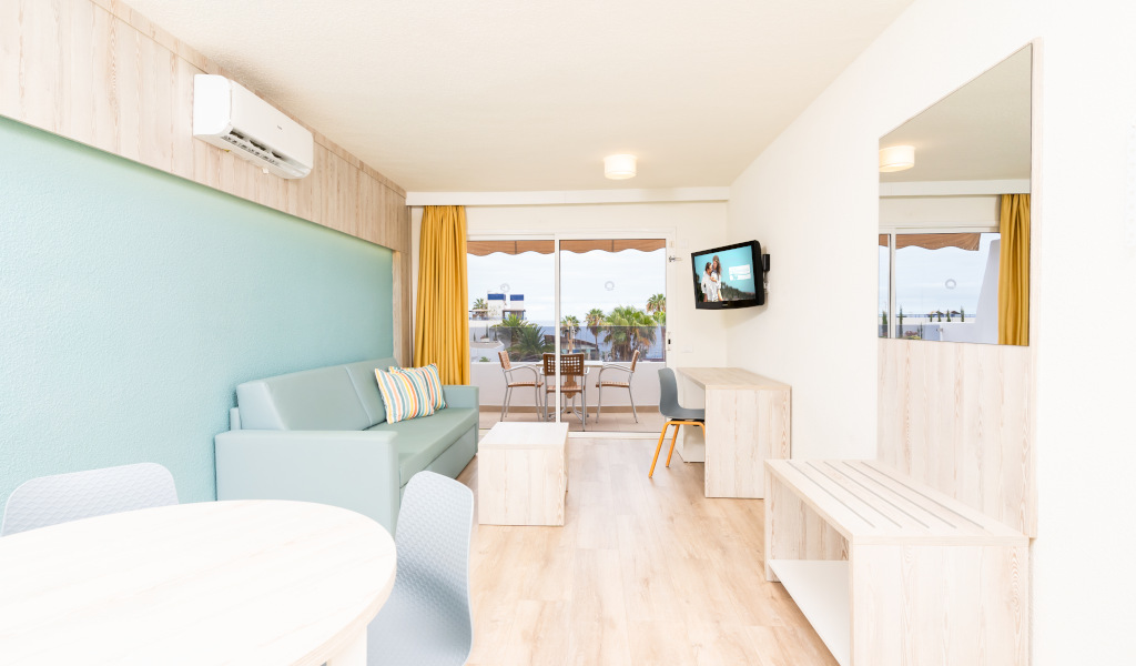 Wohnzimmer mit Sofa, Tisch, Fernseher und Balkonblick auf Los Cristianos, Teneriffa.