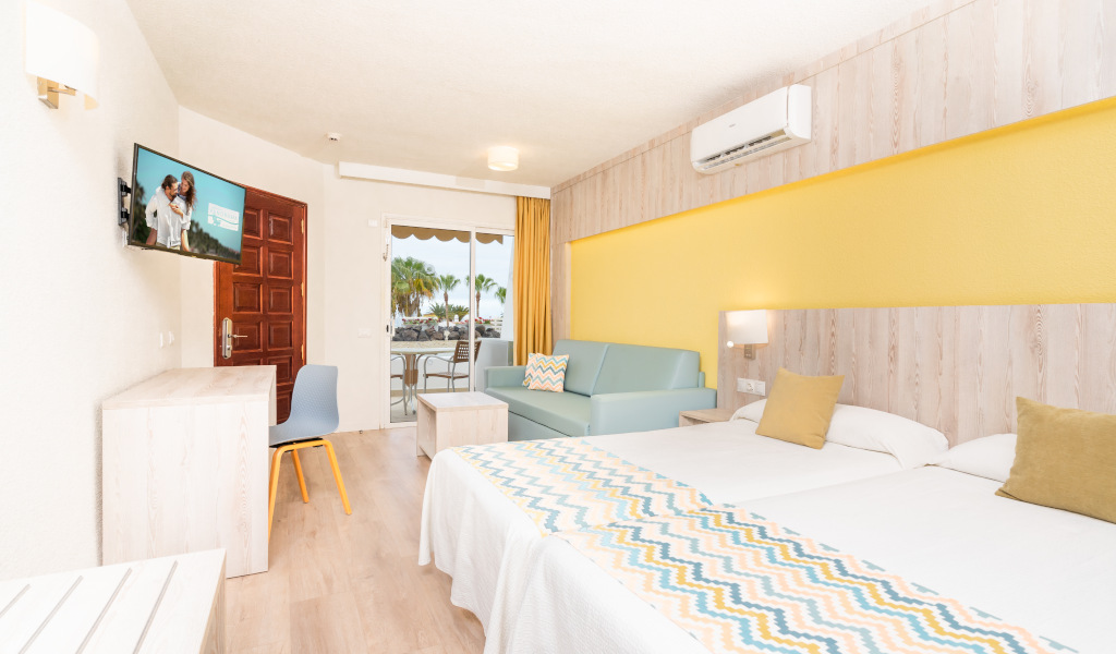 Hotelzimmer mit zwei Betten, Sofa, Fernseher und Blick auf den Balkon in Costa Adeje.