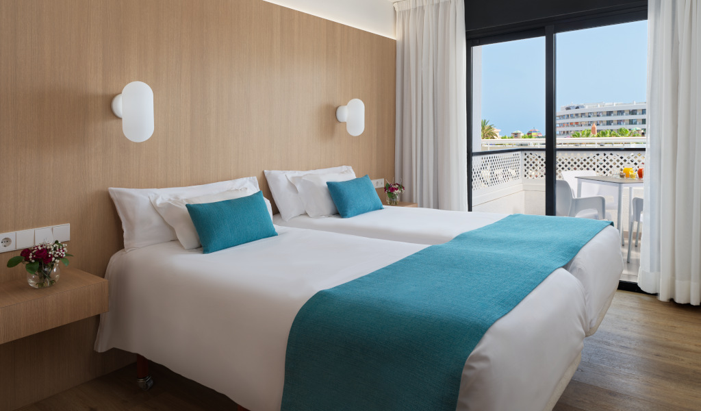 Zwei Betten mit blauen Kissen in einem Hotelzimmer in Tenerife, Balkon mit Aussicht.