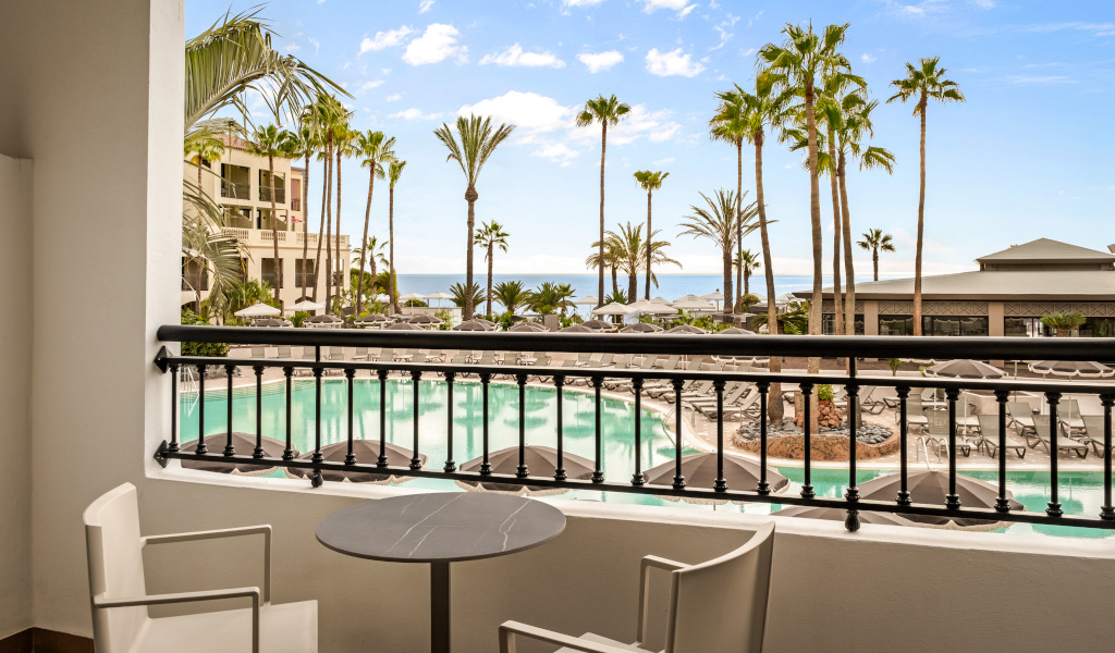 Blick vom Balkon auf Pool und Palmen in Costa Adeje, Teneriffa, mit Meereshintergrund.