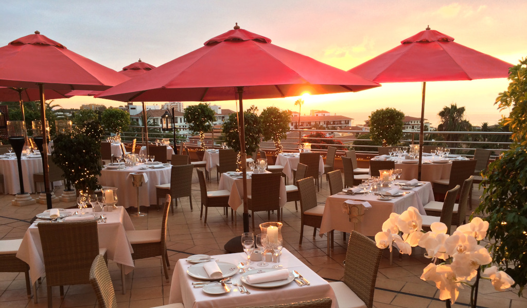 Terrasse eines Restaurants mit roten Sonnenschirmen in Costa Adeje, Teneriffa, bei Sonnenuntergang.
