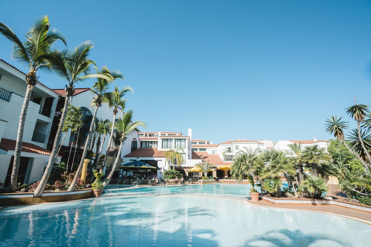 Palmen und Gebäude umgeben einen Pool in einem Resort in Tenerife.
