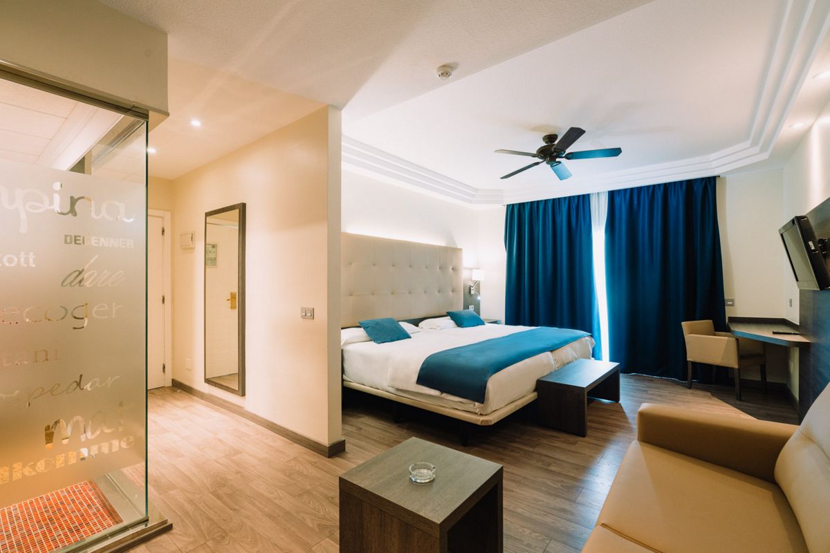 Hotelzimmer in Tenerife mit großem Bett, blauen Vorhängen, Spiegel und Schreibtisch.