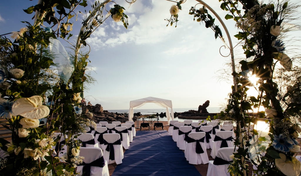 Hochzeitsaufbau am Strand von Teneriffa mit Stühlen und Blumenbogen.