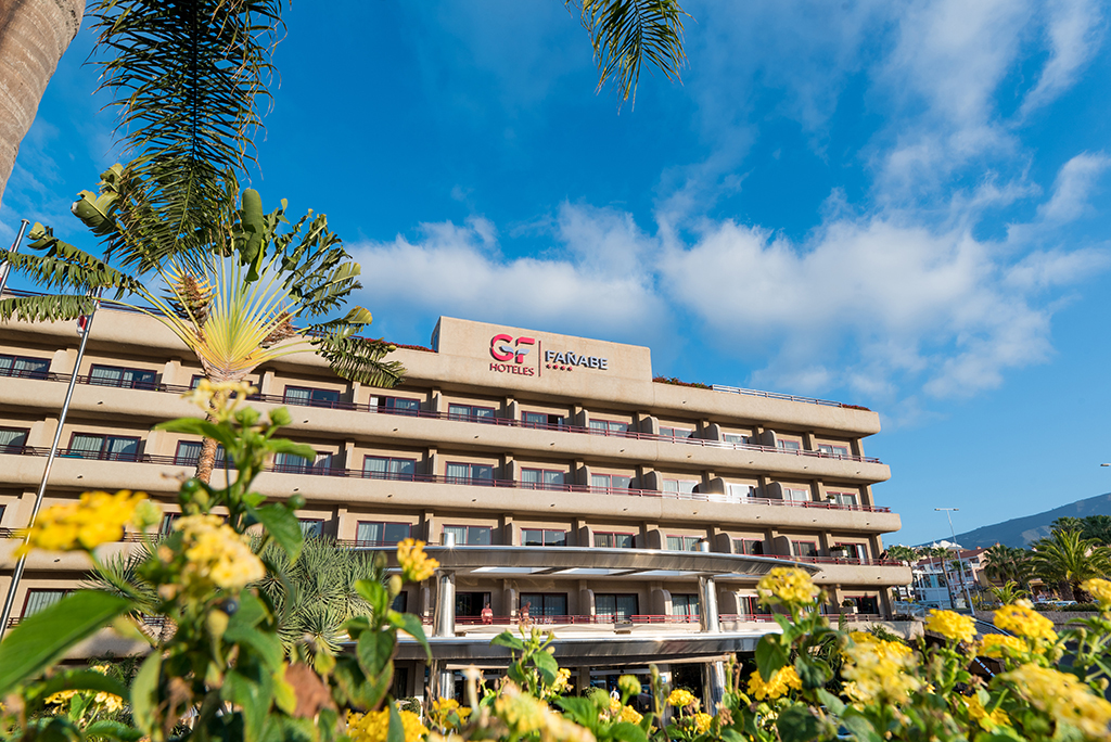 Gebäude des Hotels GF Fañabe in Costa Adeje mit gelben Blumen im Vordergrund.
