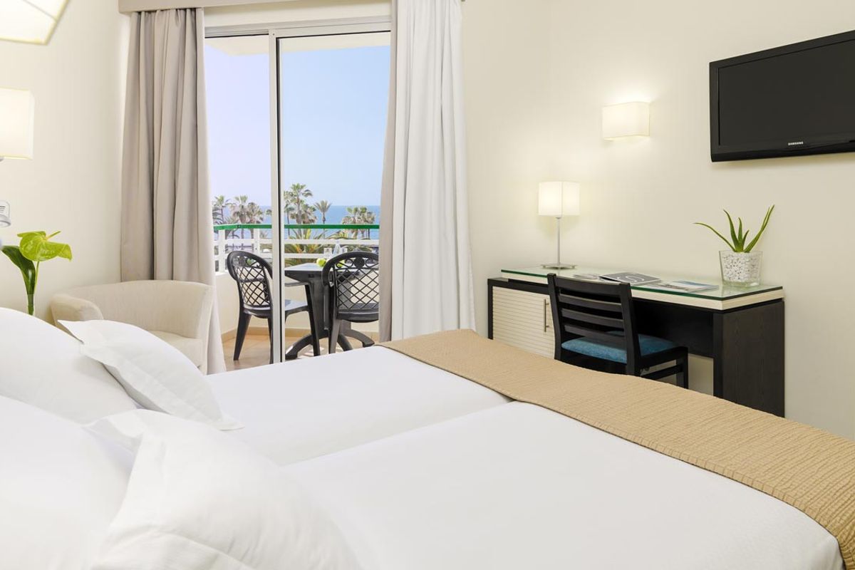 Zwei Betten und Schreibtisch in einem Hotelzimmer mit Balkon und Meerblick in Teneriffa.