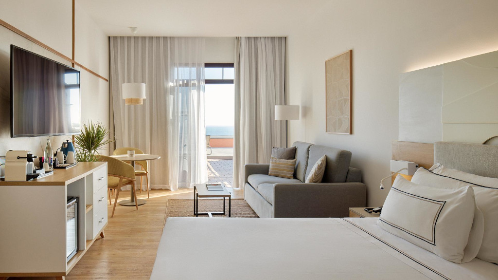 Hotelzimmer mit Bett, Sofa, Fernseher und Sicht auf den Ozean in Costa Adeje, Teneriffa.