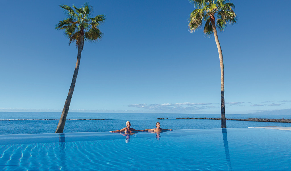 Personen entspannen in einem Infinity-Pool mit Palmen und Meerblick in Puerto de la Cruz.
