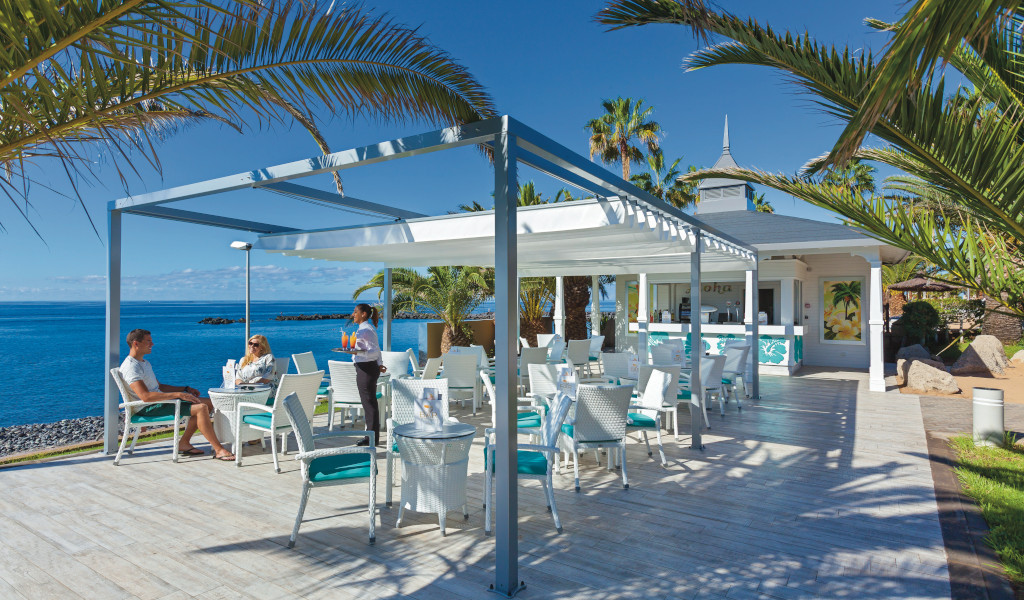 Außenbereich eines Cafés am Meer in Tenerife mit Palmen und Gästen.