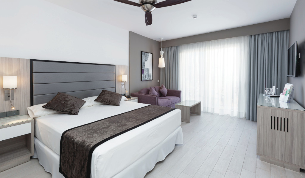 Geräumiges Hotelzimmer mit Bett, Sofa und Vorhängen in Puerto de la Cruz, Teneriffa.