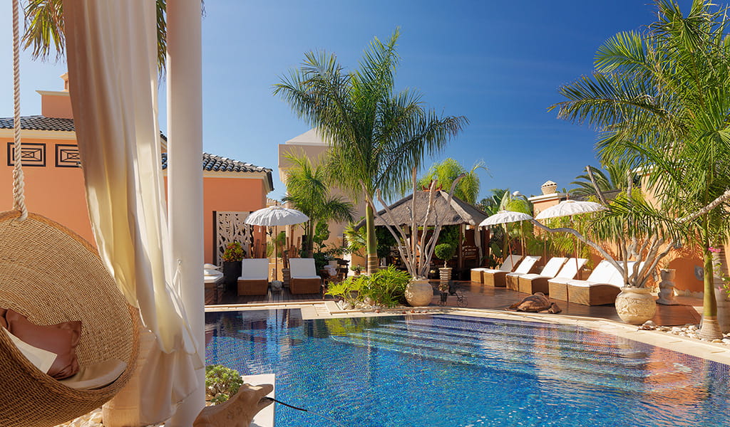 Poolbereich mit Palmen und Sonnenschirmen in Hotel auf Teneriffa.