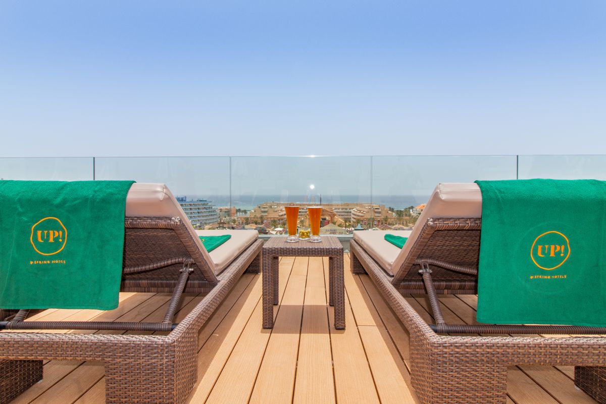 Zwei Sonnenliegen mit grünen Handtüchern und Getränken auf Dachterrasse in Teneriffa.