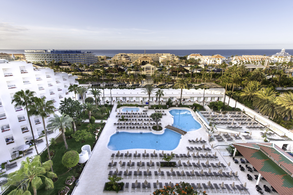 Außenansicht eines Resorts in Playa de las Américas, mit Pool, Palmen und Meerblick.