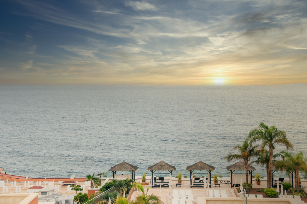Sonnenuntergang am Meer mit Palmen und Pavillons in Costa Adeje, Teneriffa.