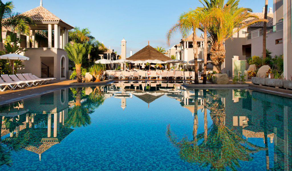 Poolbereich im Hotel auf Teneriffa mit Palmen und Liegestühlen.