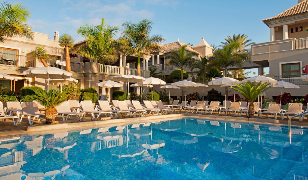 Pool und Sonnenliegen in einem Resort in Teneriffa umgeben von Palmen.