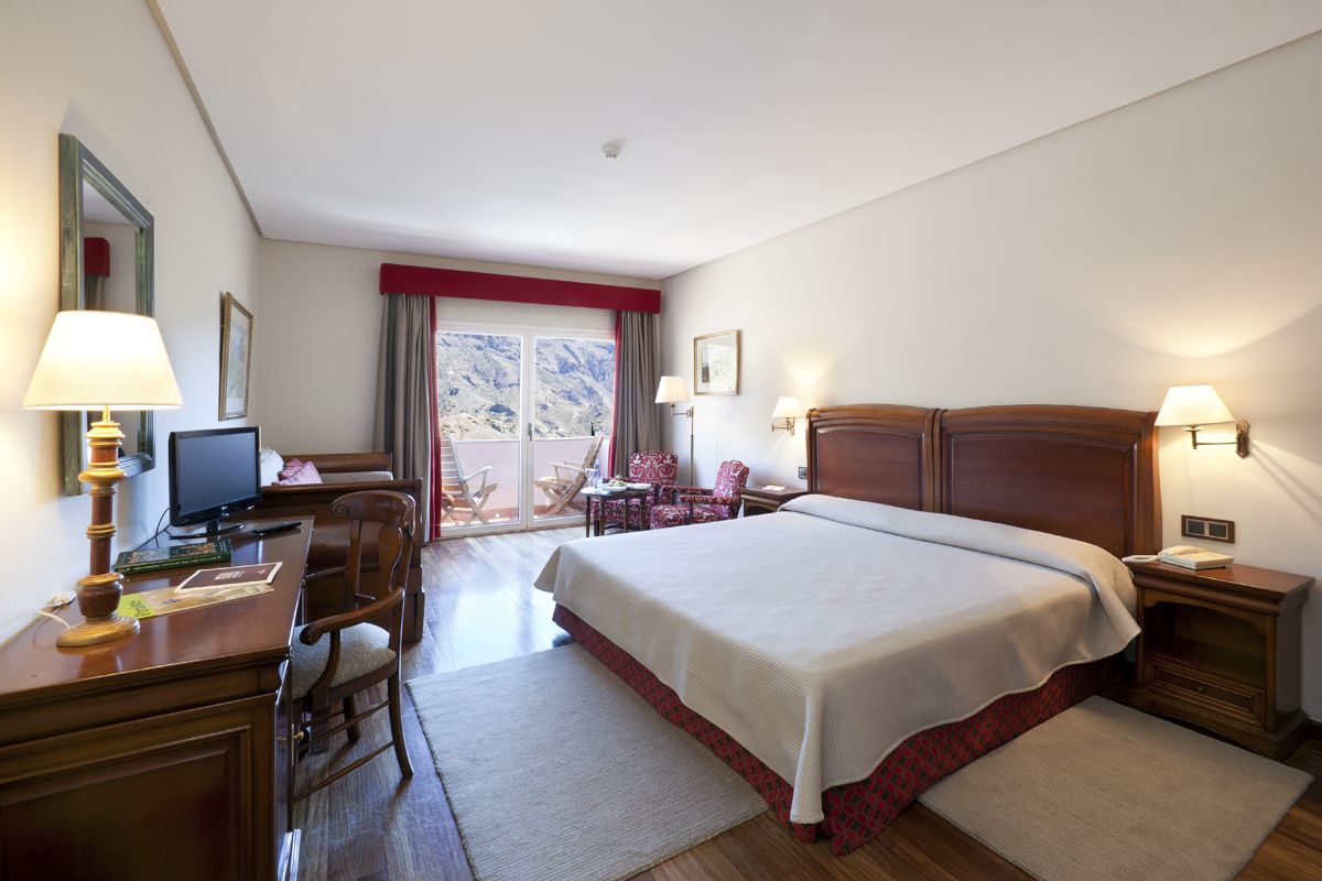 Hotelzimmer mit Doppelbett, Schreibtisch, Fernseher und Balkonblick auf Berge in Teneriffa.
