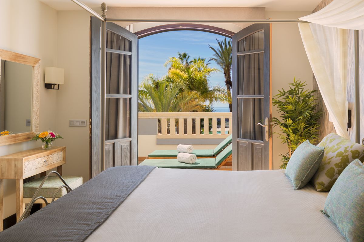 Schlafzimmer mit Balkon in Tenerife, bietet Blick auf Palmen und Liegestühle mit Handtüchern.