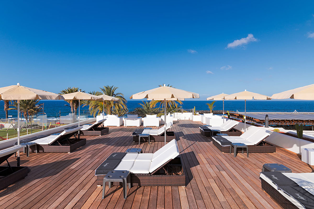 Liegestühle und Sonnenschirme auf Holzdachterrasse mit Meerblick in Puerto de la Cruz, Teneriffa.