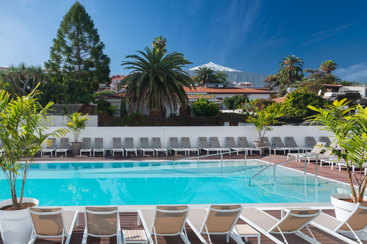 Poolbereich mit Liegestühlen vor Palmen und Teide-Berg in Puerto de la Cruz, Teneriffa.