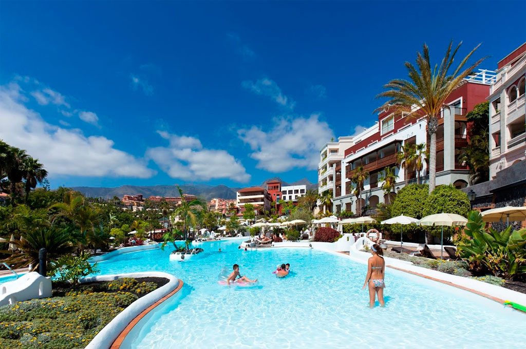 Pool mit Palmen und Gebäuden in Costa Adeje, Teneriffa. Personen im Wasser.