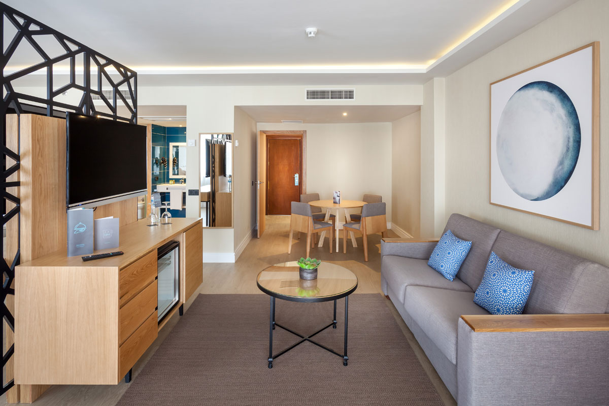Wohnzimmer mit Sofa, Tisch, Fernseher und Essbereich im Hotelzimmer in Teneriffa.