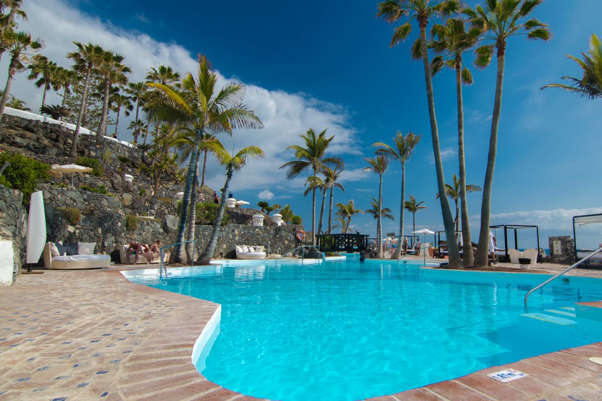 Schwimmbad mit Palmen in Costa Adeje, Teneriffa, bei sonnigem Wetter.