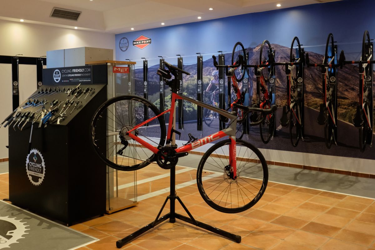 Rotes BMC-Rennrad im Geschäft auf Teneriffa, mit Zubehör und Wandbild im Hintergrund.