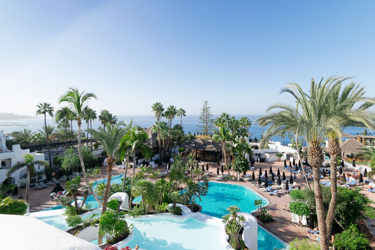 Poollandschaft mit Palmen und Blick auf das Meer in Hotelanlage in Costa Adeje, Teneriffa.