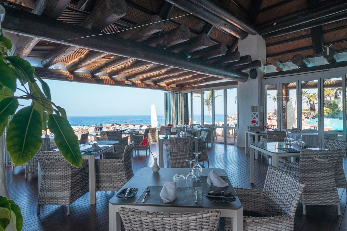 Restaurant mit Meerblick in Adeje, Teneriffa. Tische und Stühle auf Holzterrasse.