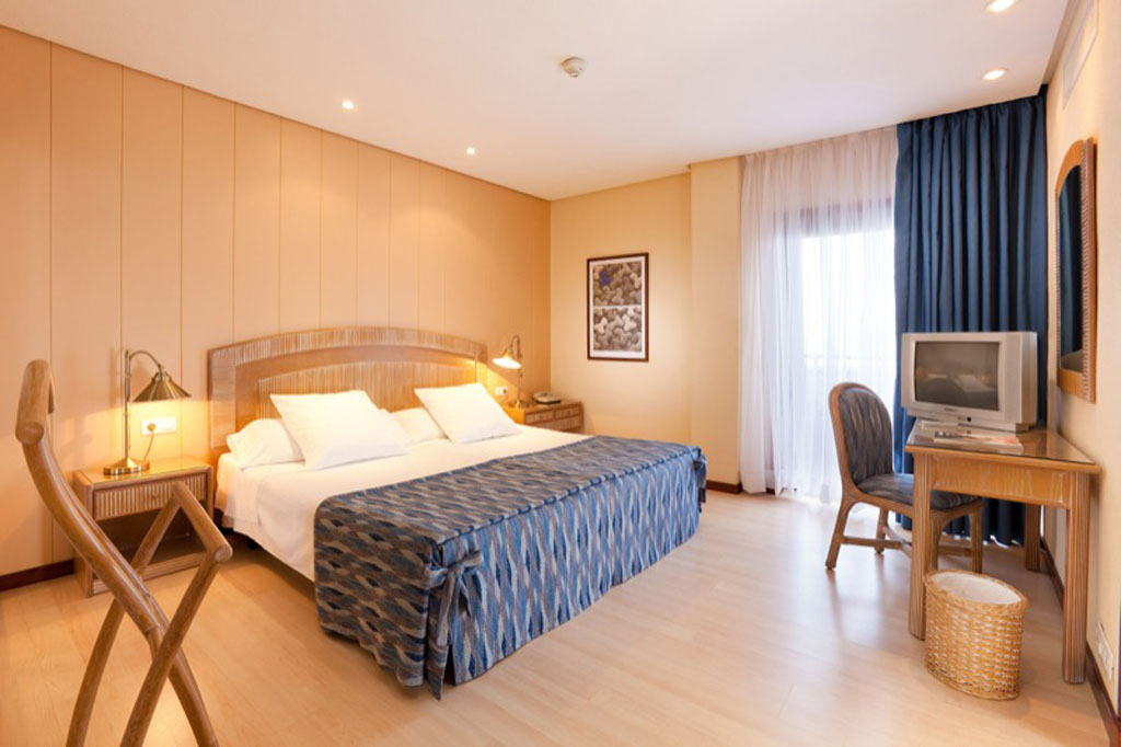 Hotelzimmer mit Doppelbett, Nachttischen, Fernseher und Fenster in Teneriffa.