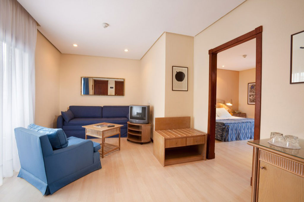 Wohnzimmer mit blauem Sofa, Fernseher und Zugang zu einem Schlafzimmer in Tenerife.