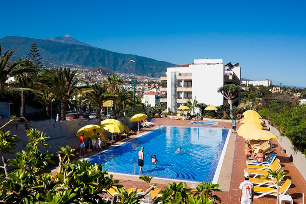 Poolbereich mit Liegestühlen und Palmen in Puerto de la Cruz, Tenerife. Hintergrund Berge sichtbar.