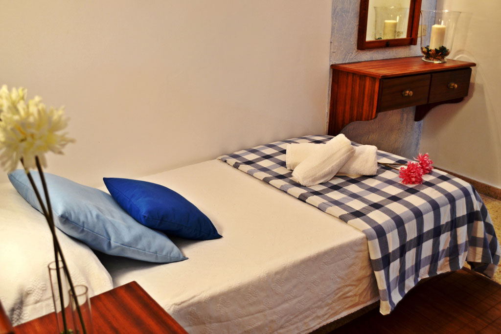 Einzelbett mit blau kariertem Überwurf und zwei Kissen, zwei Handtücher und Blume im Hotelzimmer in Tenerife.