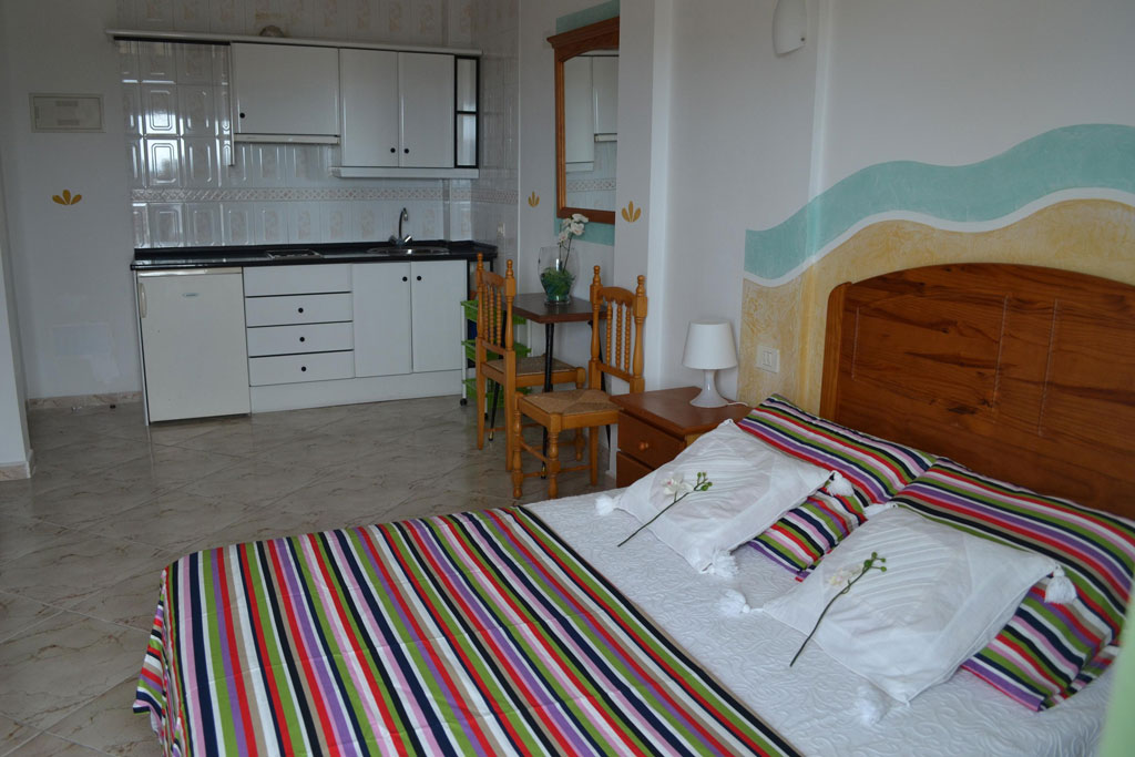 Schlafzimmer mit buntem Bett, Küchenzeile und Holzmöbeln in Teneriffa.