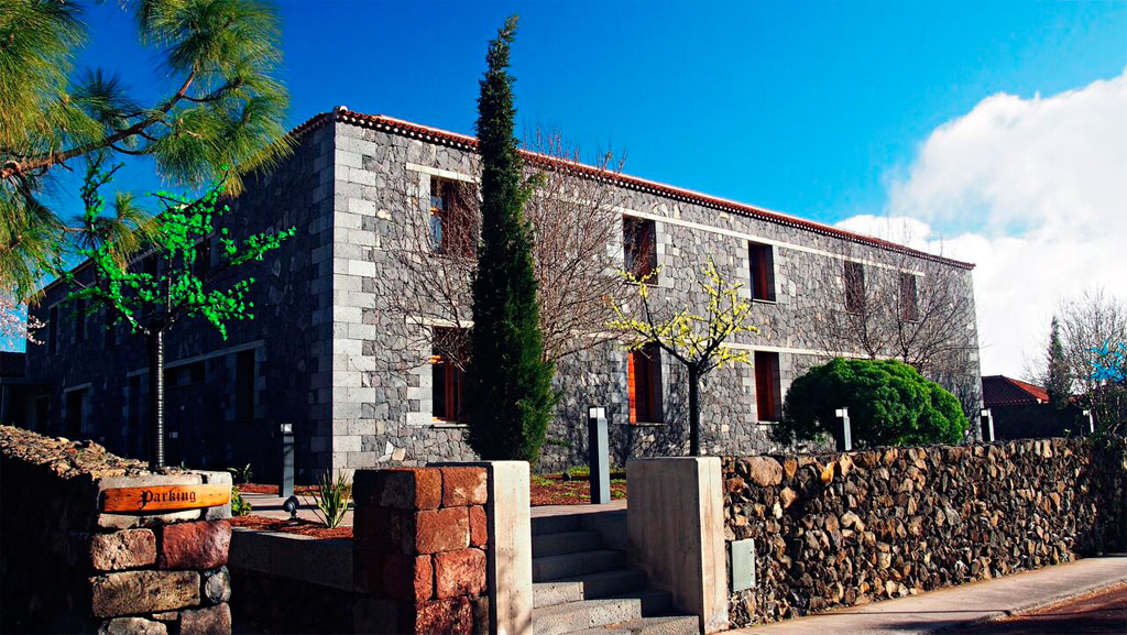 Steingebäude mit Parkplatzschild und Bäumen in Vilaflor, Teneriffa.
