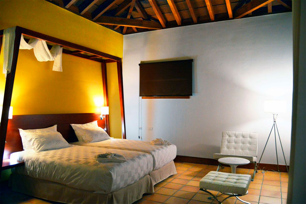 Bett in einem Hotelzimmer in Teneriffa mit moderner Einrichtung und Holzbalkendecke.