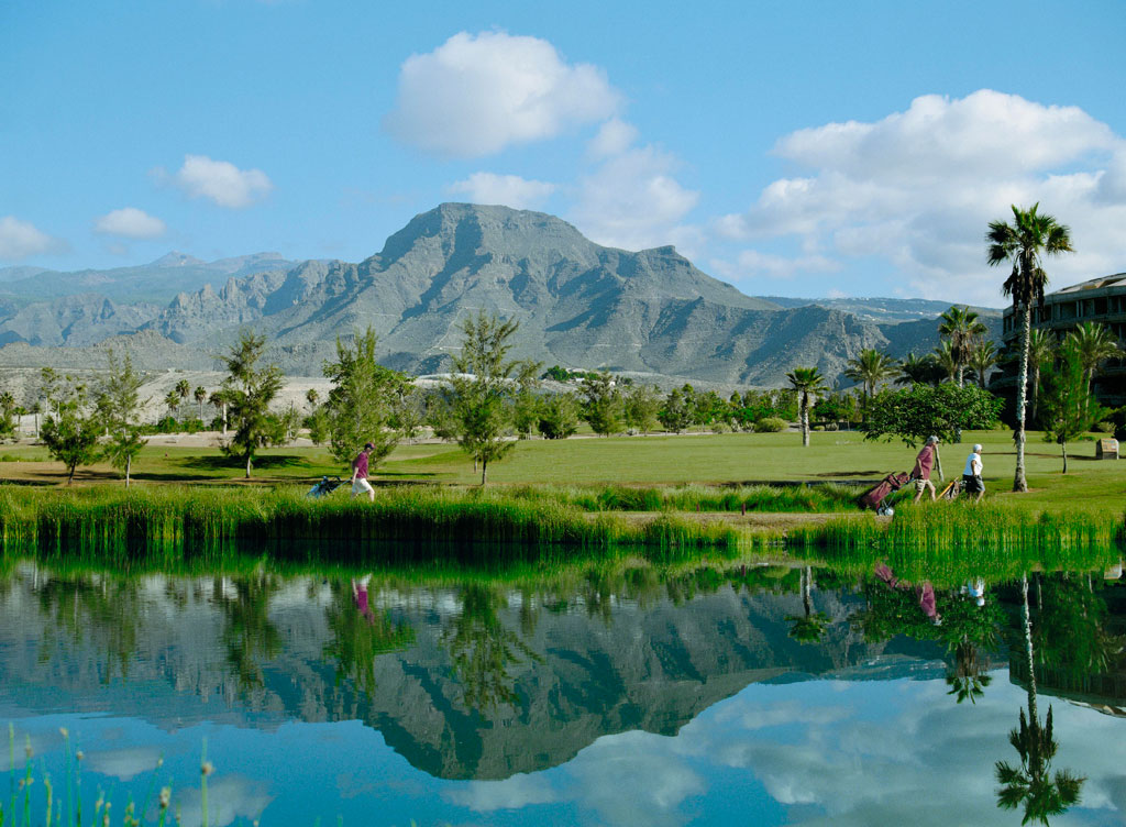 Golfspieler auf einem Platz in Teneriffa vor einem Berg und einem See.