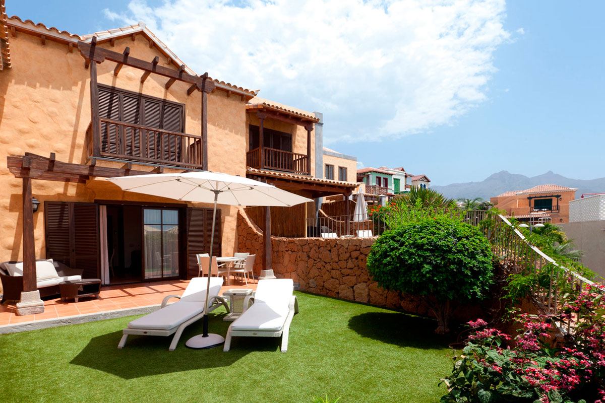 Zweistöckiges Haus mit Liegestühlen und Sonnenschirm im Garten in Tenerife.