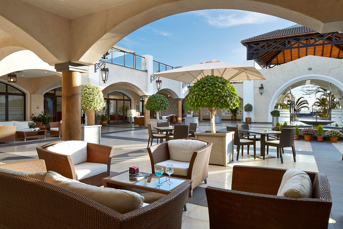 Überdachte Terrasse eines Cafés in Santa Cruz de Tenerife mit Rattanmöbeln und Pflanzen.