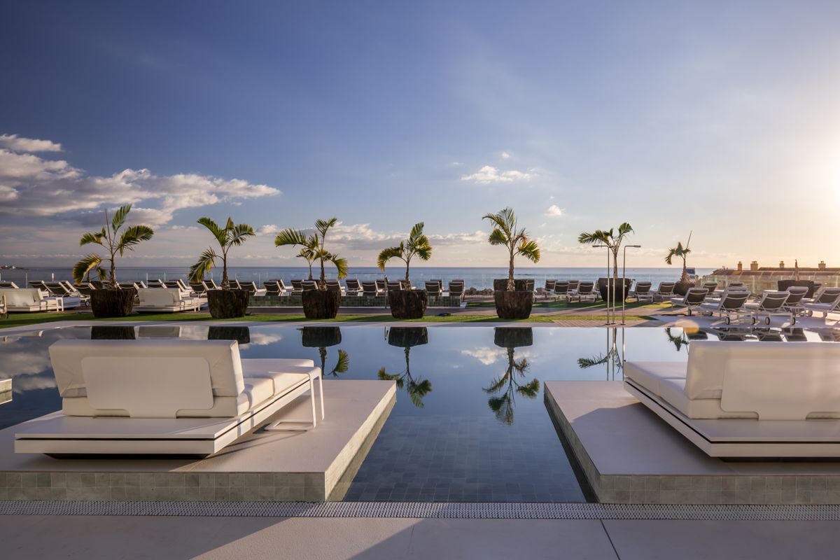 Sonnenliegen und Palmen am Pool mit Meerblick in Arona, Teneriffa.
