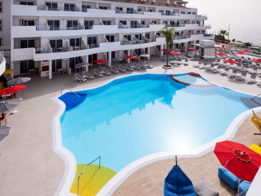 Schwimmbad, umgeben von Sonnenliege und Sonnenschirmen in einem Touristenzentrum auf Teneriffa.