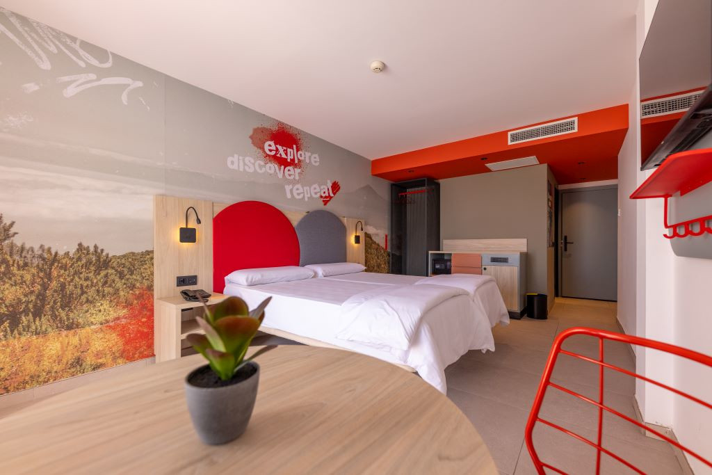 Modernes Zimmer mit Doppelbett, Grundriss und Wandgemälde, auf dem steht: Entdecken, entdecken, wiederholen.